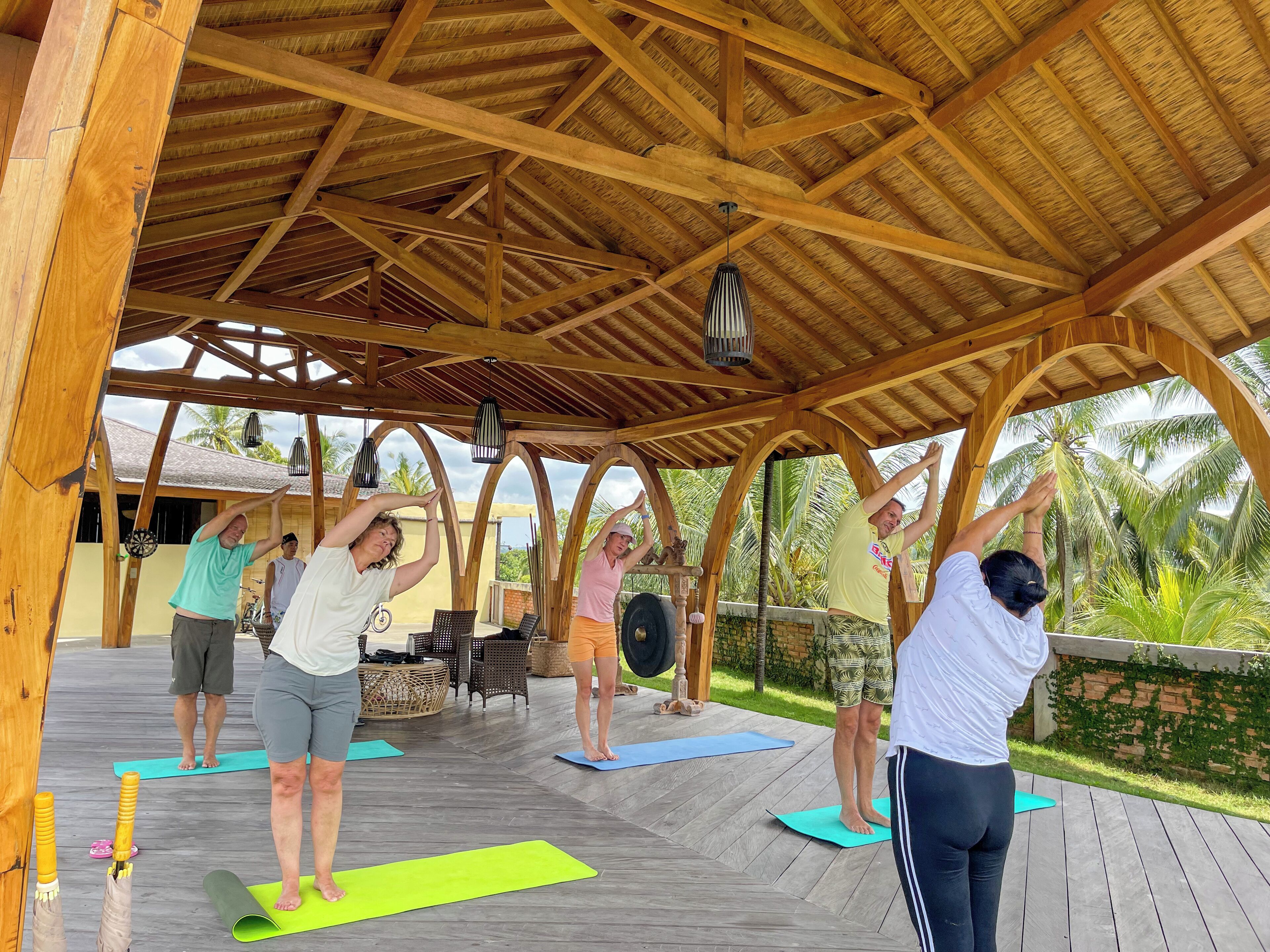 Een houten terras met rieten dak, yogamatten en fitnessapparatuur.