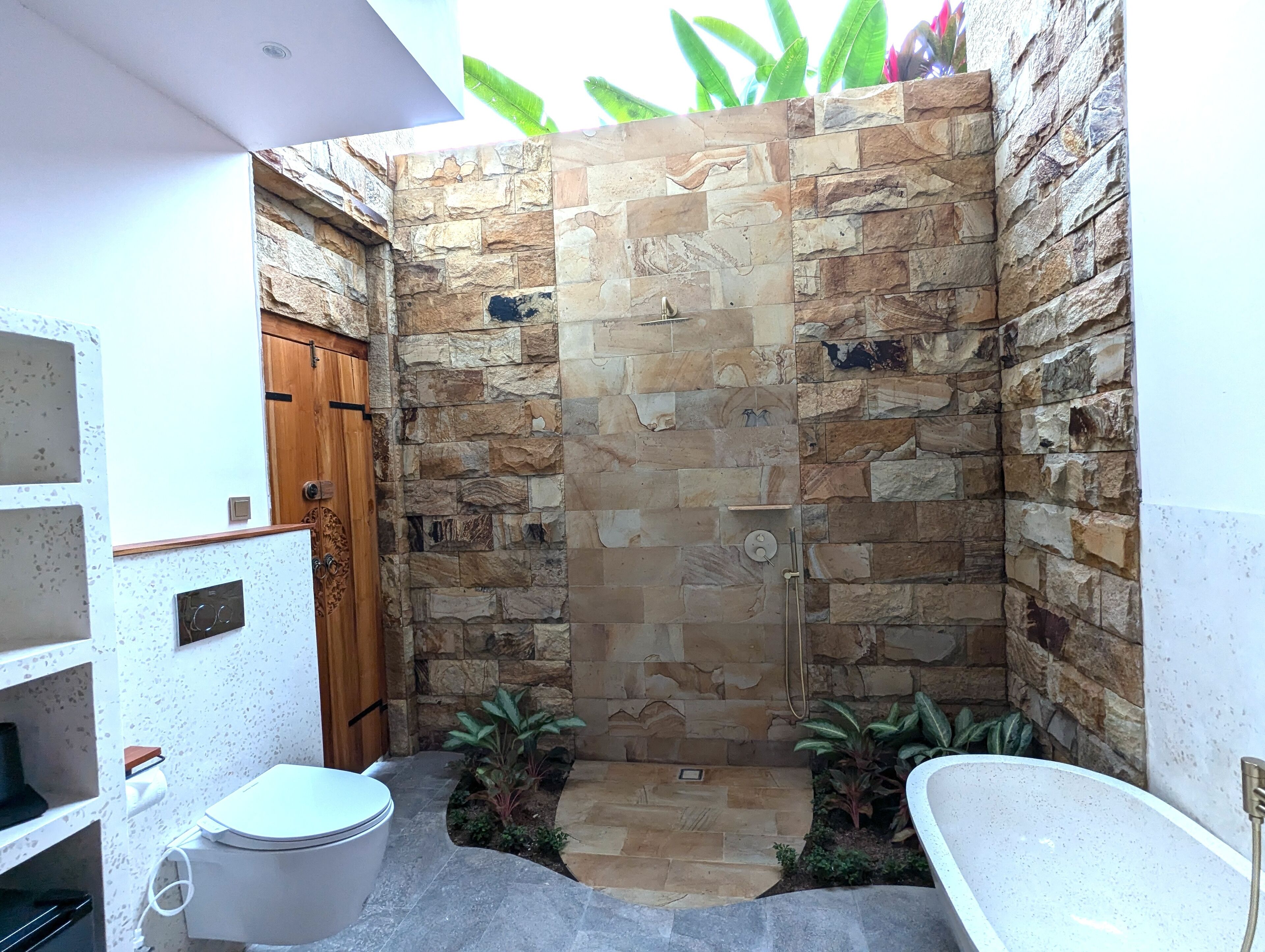 Une salle de bain avec une douche à l’italienne en pierre, des toilettes et une baignoire.
