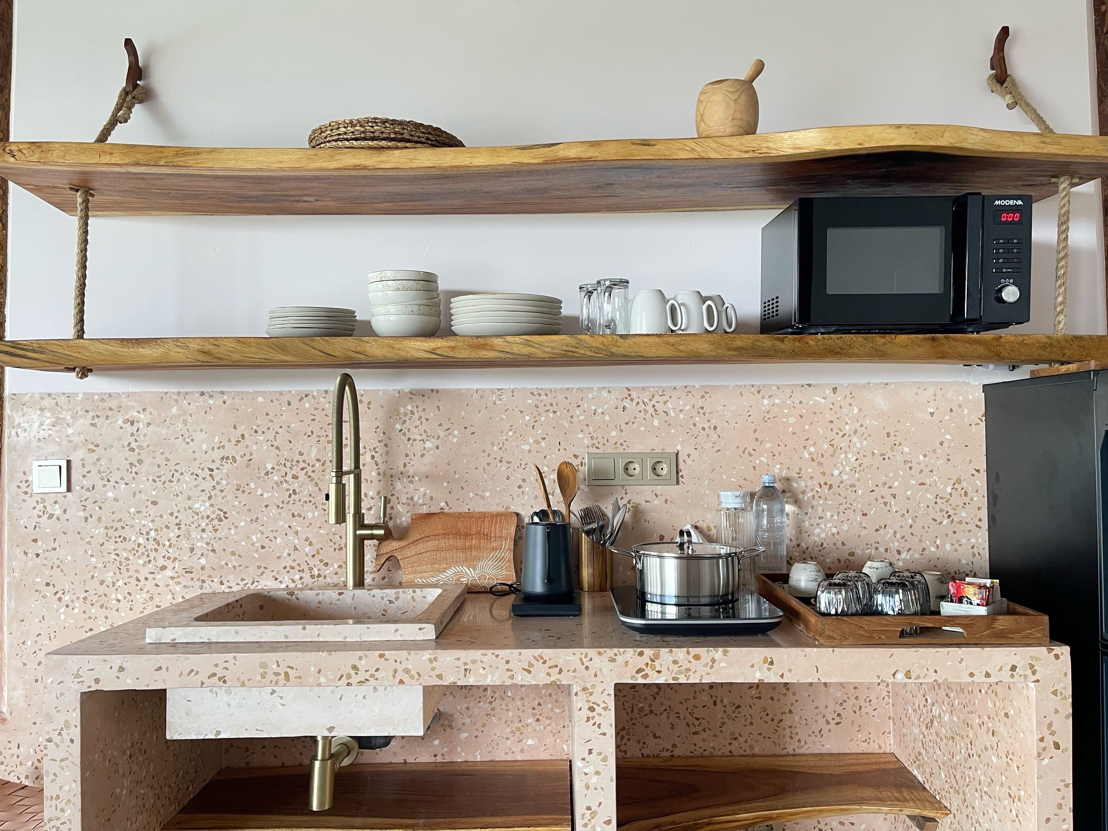 Una cocina con encimera de granito, pileta de acero inoxidable y microondas sobre una repisa de madera.
