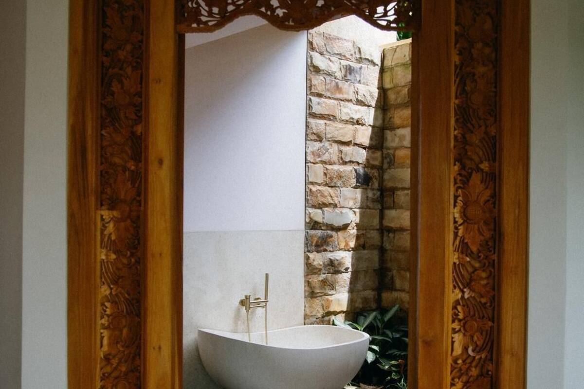 An entrance with a wooden door leading to a bathroom with a stone wall and a freestanding bathtub.