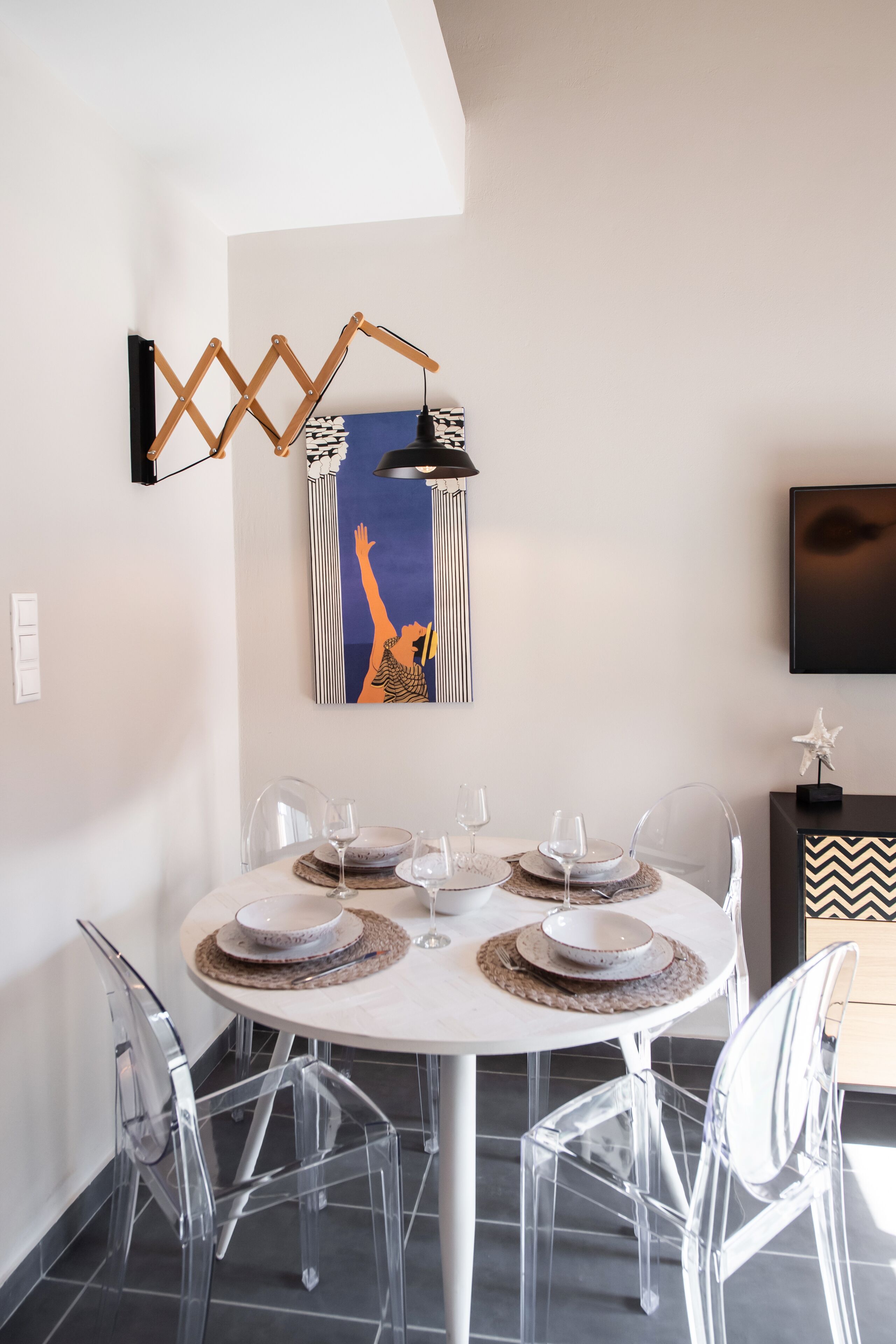 Un comedor con una mesa redonda, sillas traslúcidas y una lámpara fijada a la pared.