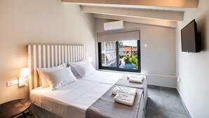 A hotel room with a large bed, a small table, a window with a view of buildings, and a mounted TV. - Gateway in Lefkada (Lefkada)