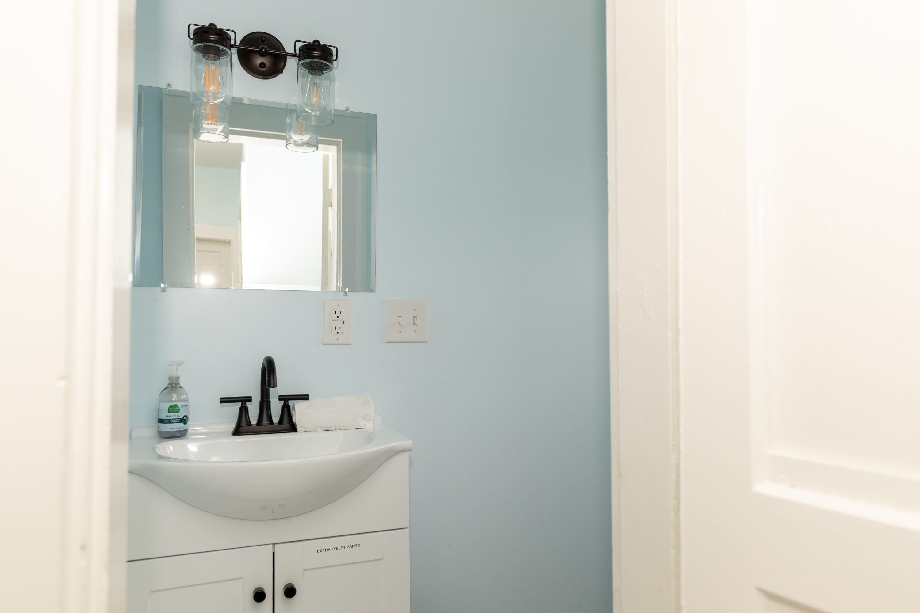 A bathroom with a white sink, a mirror, and a bottle of hand soap.