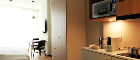 Une chambre d’hôtel de taille réduite, comprenant un lit, un bureau, une kitchenette et un téléviseur fixé au mur.