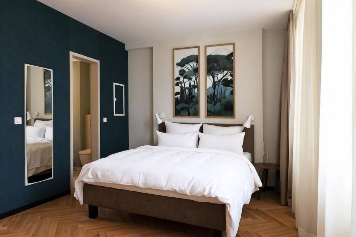 A bedroom with a large bed, a mirror, and two framed pictures on the wall.