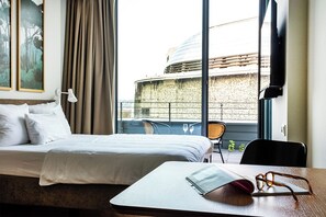 A hotel room with a bed, a table with glasses, and a view of a building through large windows. - Hood House Kassel (Kassel)