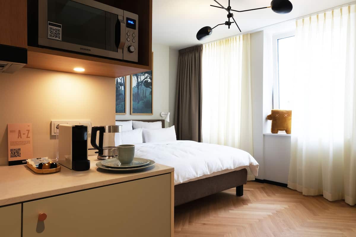 A hotel room with a bed, a desk with a coffee maker, a microwave, and a window with curtains.