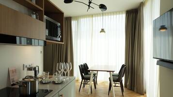 A modern kitchen with a built-in stove, microwave, and shelves. There is a dining area with a table and chairs, and a large window with curtains.
