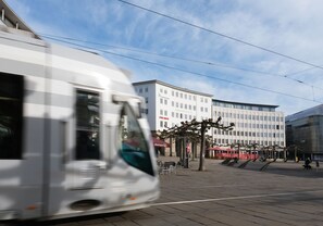 A tram moving past a modern building with a sign that reads "KONIGSPLAZAT". - Hood House Kassel (Kassel)