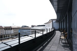 Terraza en la azotea con vistas a la ciudad, que incluye una barandilla y varias sillas de mimbre.
