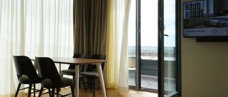 Une pièce moderne avec une table et des chaises en bois, de grandes fenêtres ornées de rideaux légers et une porte-fenêtre coulissante donnant sur un espace extérieur.