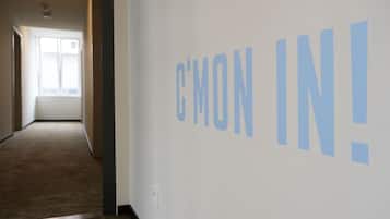 Un pasillo con una pared que muestra el texto 'C'MON IN!' y una ventana al final.
