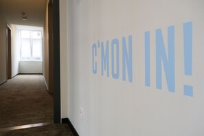Un couloir avec un mur sur lequel est inscrit le texte « ENTREZ ! » et une fenêtre au fond.
