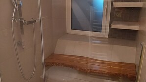 Une douche fermée par des parois de verre, avec un sol carrelé, un banc en bois et une fenêtre visible.