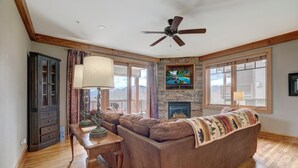 A living room with a stone fireplace, a large sectional sofa, a wooden coffee table, and a ceiling fan.