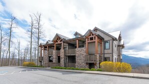 A modern multi-story building with stone and wood exterior, multiple balconies, and a parking lot.