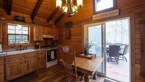 Interieur van een houten chalet met een keuken, eethoek en een schuifdeur naar een terras.
