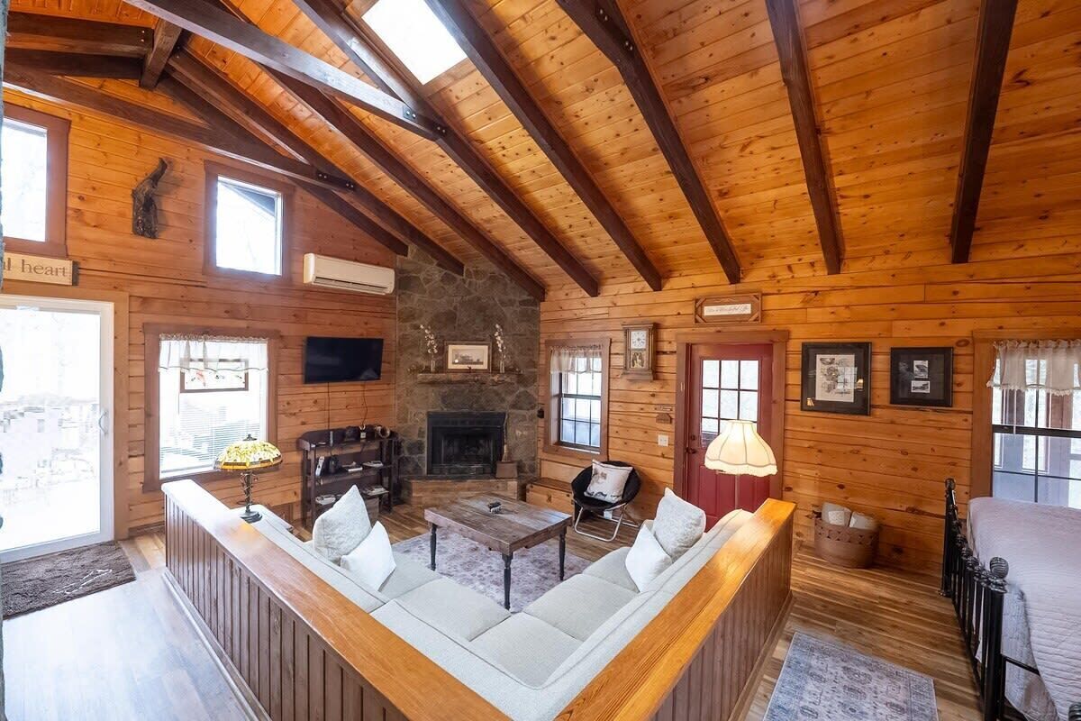 Een gezellig cabin interieur met een stenen openhaard, houten balken, een bank en een televisie.