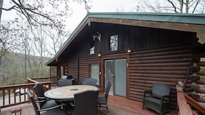 Een houten hut met een terras, een ronde tafel en stoelen.