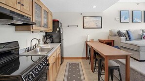 Cuina compacta amb armaris de fusta, fogó i microones. Zona de menjador amb taula i cadires, i un sofà a l'espai de sala d'estar.