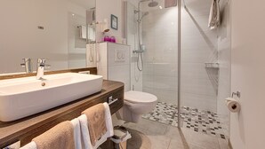 Un baño moderno con un lavamanos grande de color blanco, un box de ducha con paredes de cristal y un inodoro.