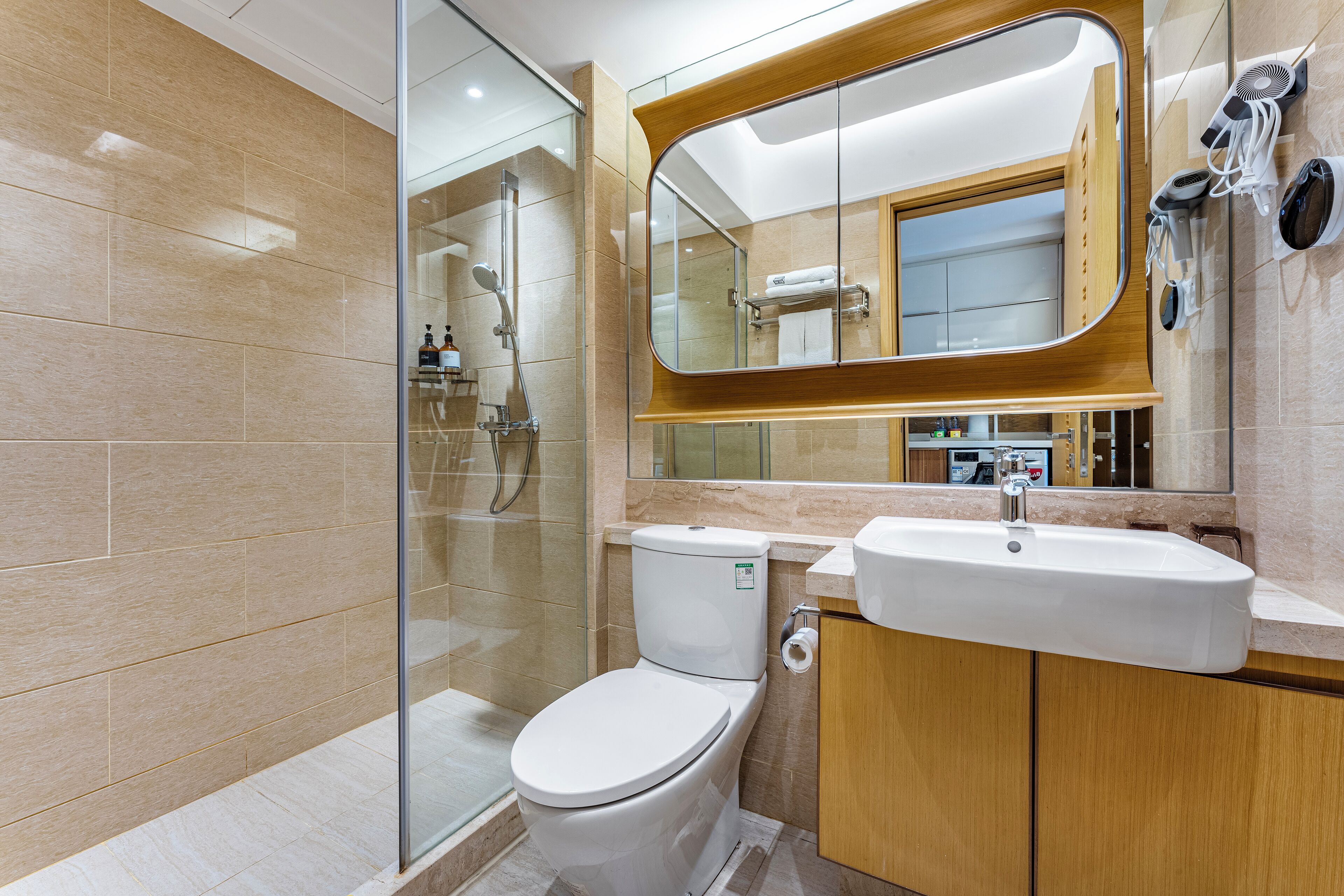 A modern bathroom with a glass shower enclosure, a white toilet, a sink, and a wooden vanity.