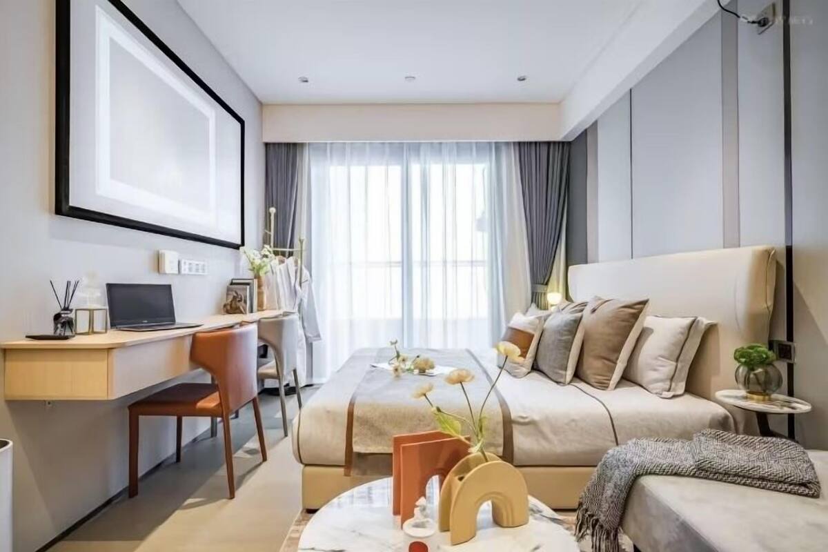 A modern hotel room with a large bed, a desk with a laptop, a chair, and a small side table.