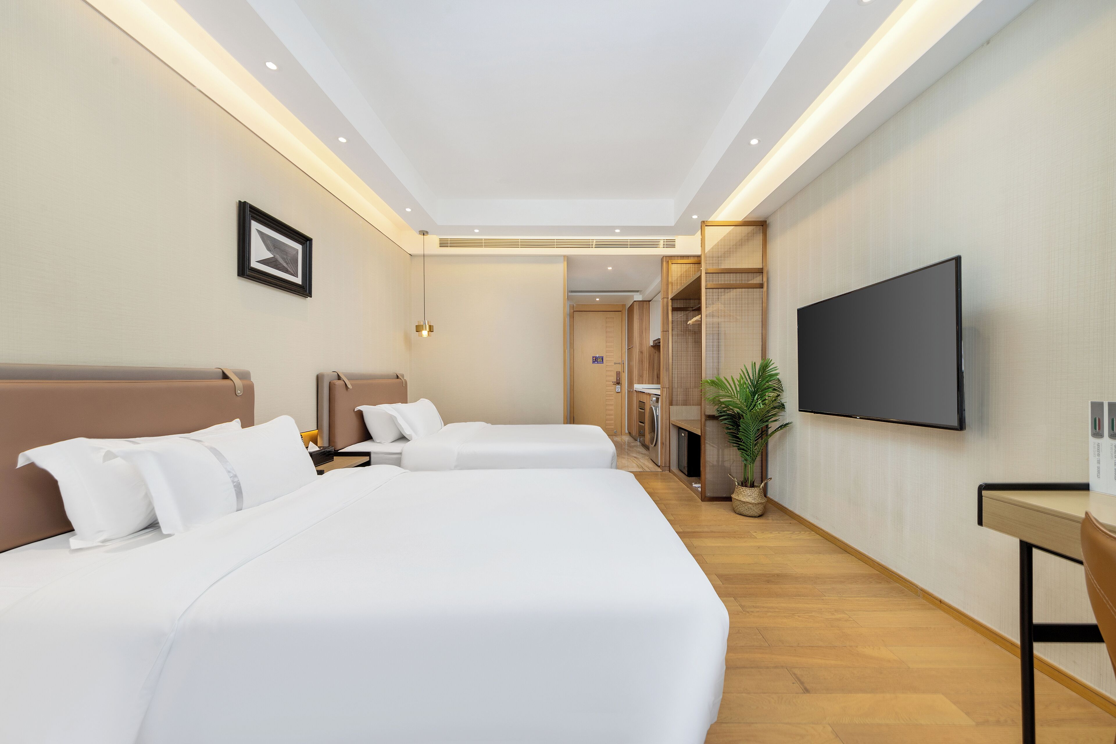 Ein Hotelzimmer mit zwei Betten, einem Fernseher, einem Schreibtisch und einer Zimmerpflanze.