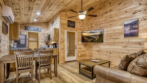 A cozy cabin interior with a dining area, a sofa, a ceiling fan, and wooden walls.