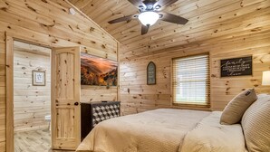 Ein gemütliches Schlafzimmer in einer Holzhütte mit einem Bett, einem Deckenventilator, einem Fenster mit Jalousien und einem an der Wand befestigten Schild.