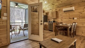 A wooden cabin interior with a dining area, kitchen, and a sliding glass door leading to a balcony. - Kerri's Cottage, Pickleball Court, Creek, WIFI, No Cleaning Fee (Cosby)