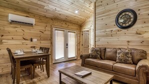 A cozy room with wooden walls, a brown leather sofa, a wooden coffee table, and a dining table with chairs. - Kerri's Cottage, Pickleball Court, Creek, WIFI, No Cleaning Fee (Cosby)