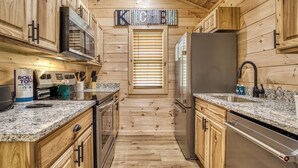 A wooden cabin-style kitchen with a granite countertop, stainless steel appliances, and a 'Kitchen' sign above the window. - Little Haven Cottage-Pickleball Court, WIFI, budget friendly (Cosby)