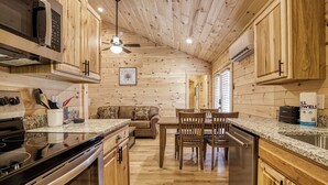 A kitchen with wooden cabinets, a stove, and a dining area with chairs and a table. - Little Gem Cabin, Pickleball Court, Creek, WIFI, Mountain Views, Starting at $79 (Cosby)
