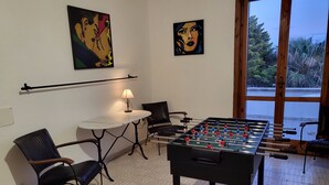 A room with a foosball table, two chairs, a small table with a lamp, and two paintings on the wall. - Villa Irene Nice Seaview (Lecce)