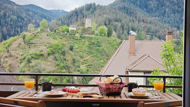 A table with breakfast items, a glass of orange juice, a black mug, a basket of bread, and a plate with a sandwich. - Schwarzwaldraum Schlossblick (Hornberg)