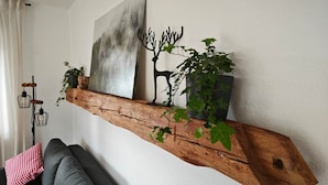 A rustic wooden shelf with plants and a painting, a gray sofa, and a black metal sculpture against a white wall. - Schwarzwaldraum Schlossblick (Hornberg)