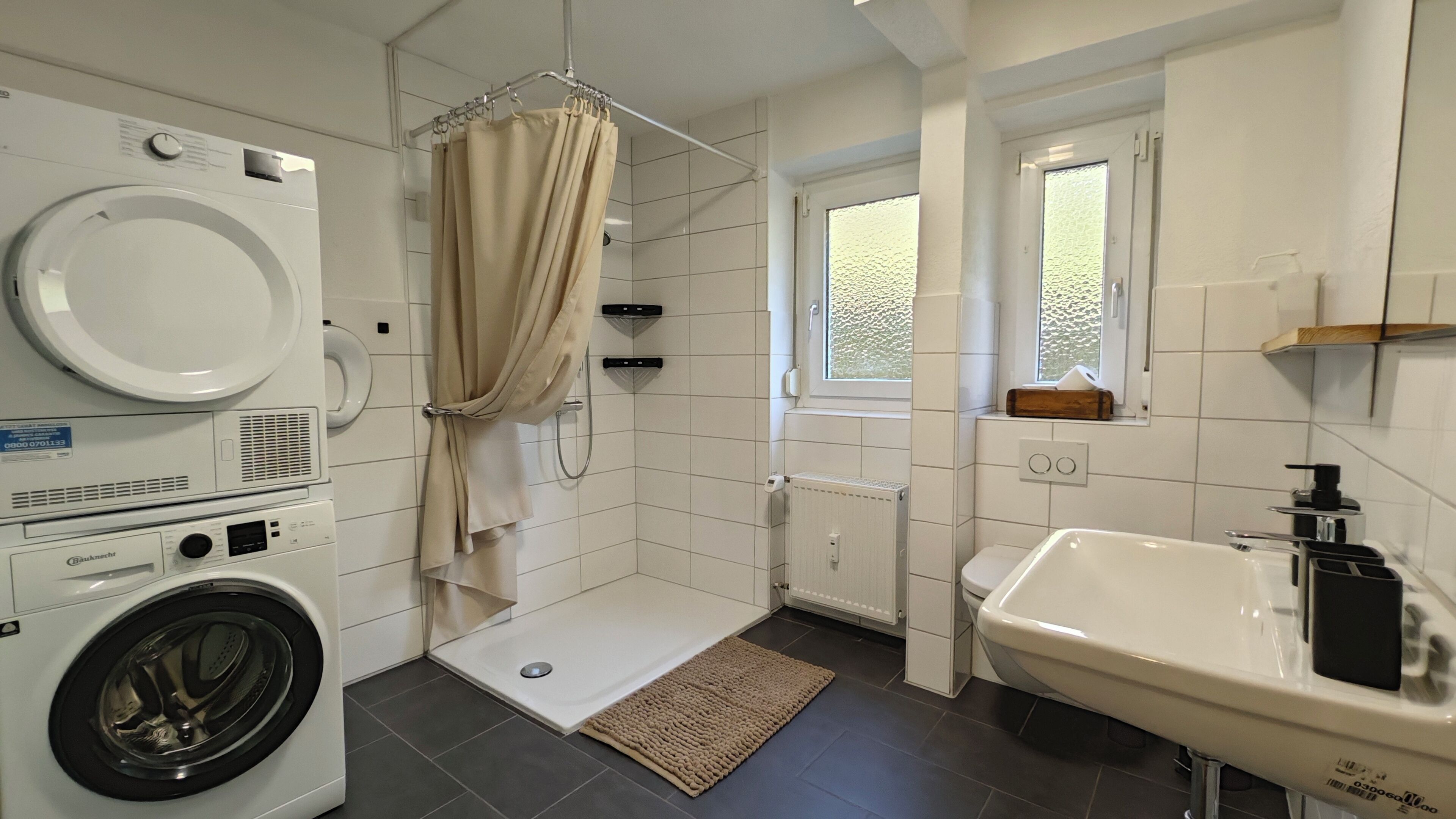 A modern bathroom with a washing machine, a shower, a sink, and a window.