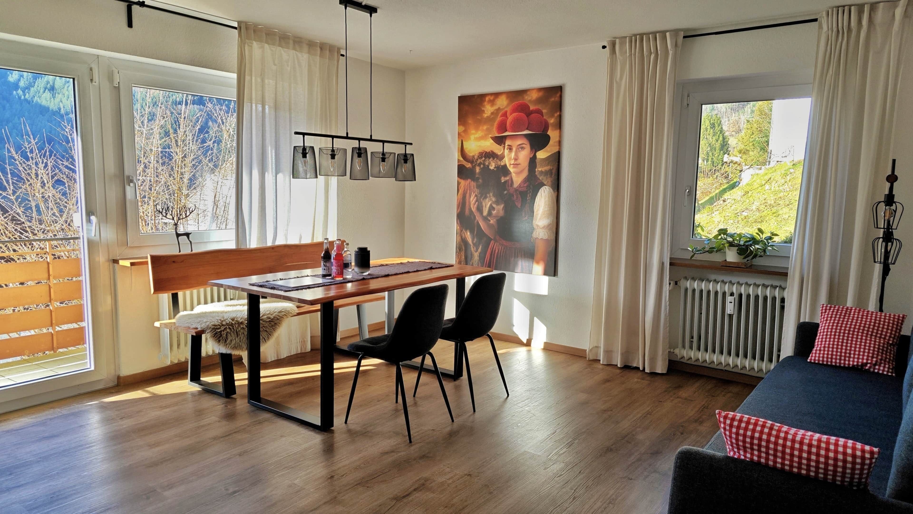 Ein Essbereich mit einem Holztisch, schwarzen Stühlen und einer Bank. Es gibt eine Heizung, ein Fenster mit Vorhängen und eine Wandleuchte.