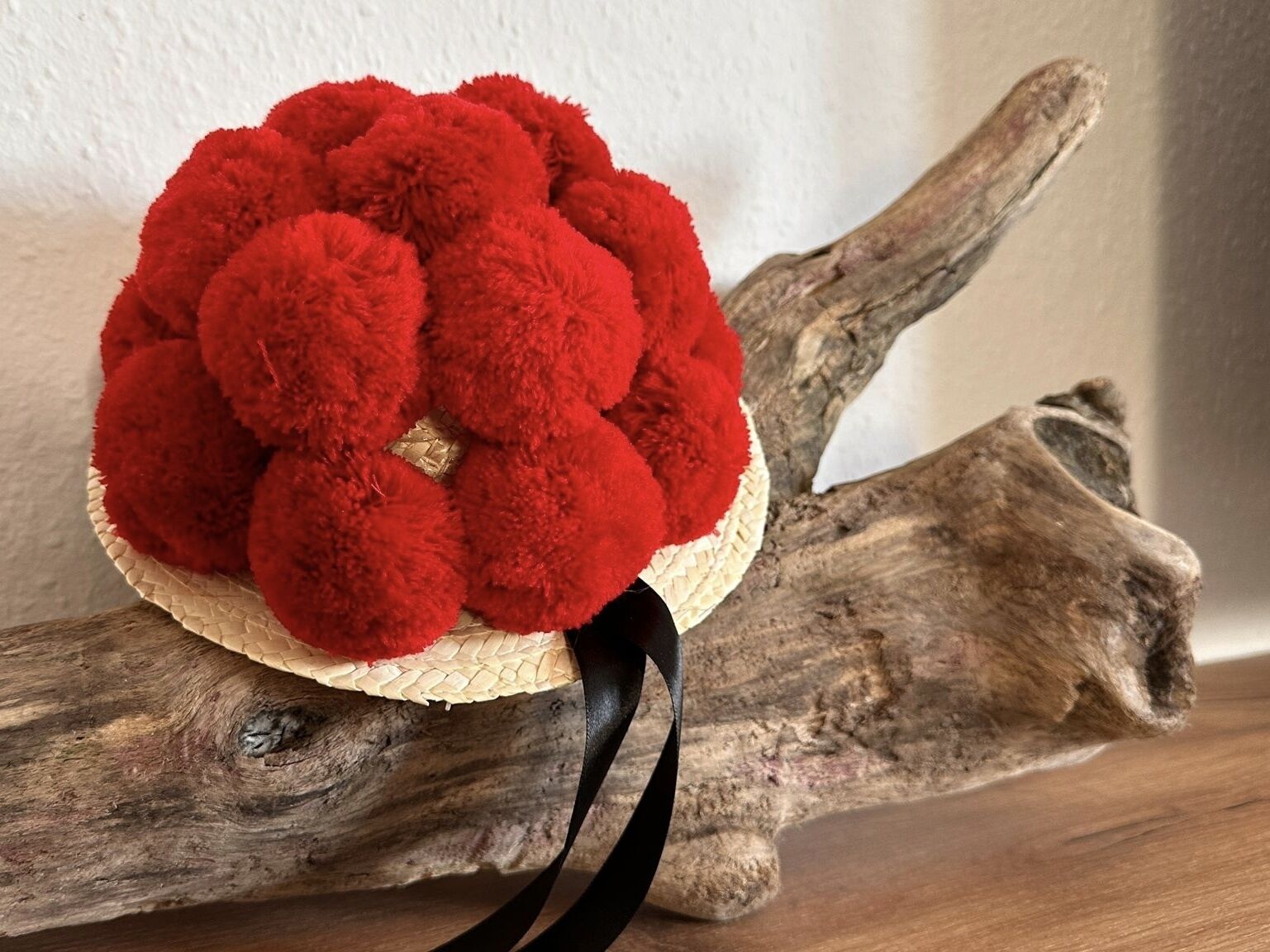 A red pom-pom ball on a woven basket placed on a wooden branch.