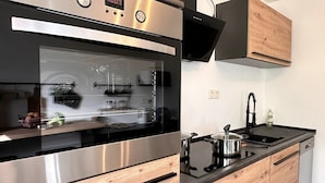 A modern kitchen with a stainless steel oven, wooden cabinets, and a black stovetop. - Schwarzwaldraum Schlossblick (Hornberg)