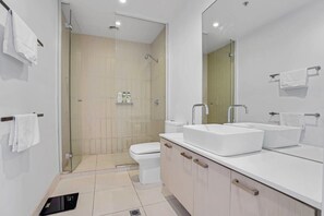 Un baño moderno con cabina de ducha de vidrio, un lavamanos blanco y un inodoro.