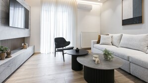 A modern living room with a sofa, two round tables, a black chair, and a TV mounted on a marble wall. - Deluxe & Upscale Apartment in Athens (Athens)