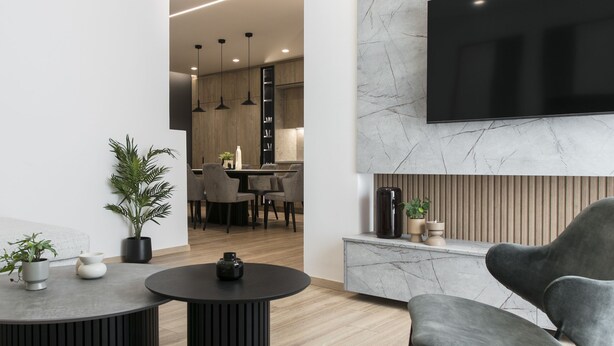 A modern living room with a flat-screen TV mounted on a marble wall, a round black coffee table, and a grey sofa. - Deluxe & Upscale Apartment in Athens (Athens)