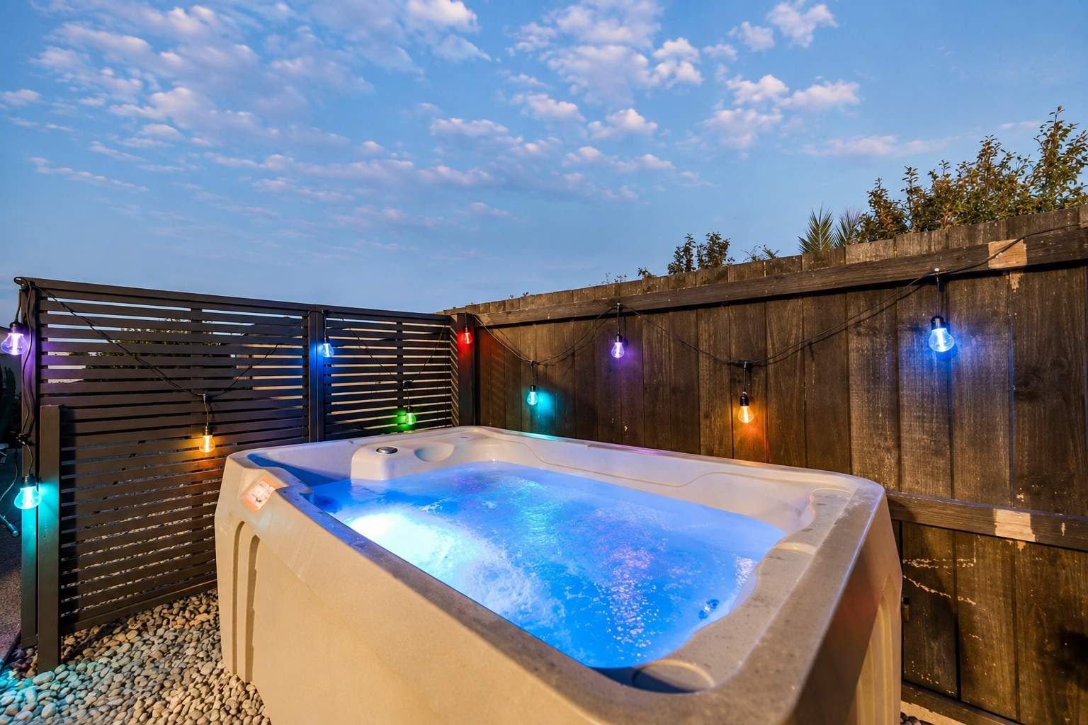Een hottub met een houten omheining en sfeerverlichting op de achtergrond.