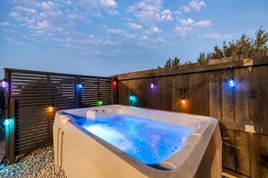 Un bain à remous entouré d’une clôture en bois, avec des guirlandes lumineuses en arrière-plan.
