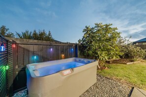 A hot tub in a backyard with a wooden fence and a tree. - Zenith Escapes Your Quintessential 4BR Haven (Christchurch)