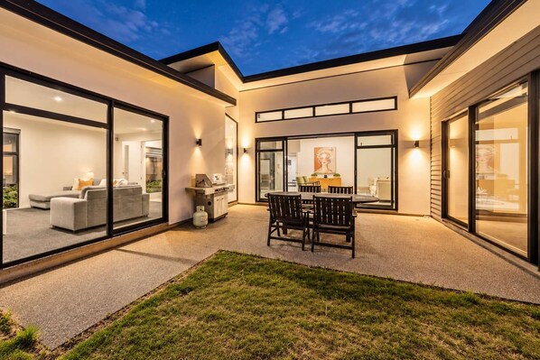 Une maison moderne dotée d’un patio, d’un espace salon extérieur et d’un coin barbecue.