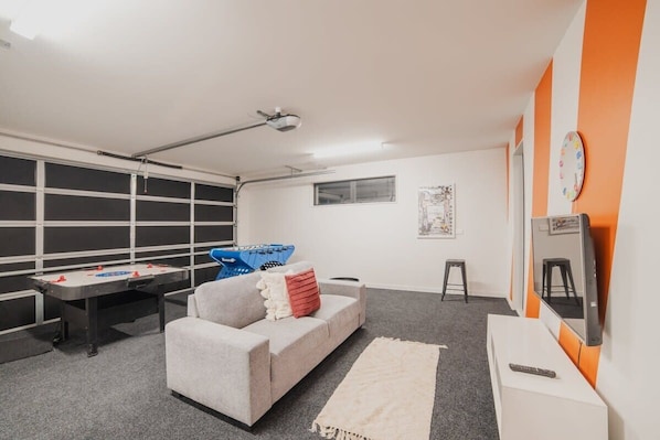 A room with a sofa, a foosball table, a desk, and a TV.