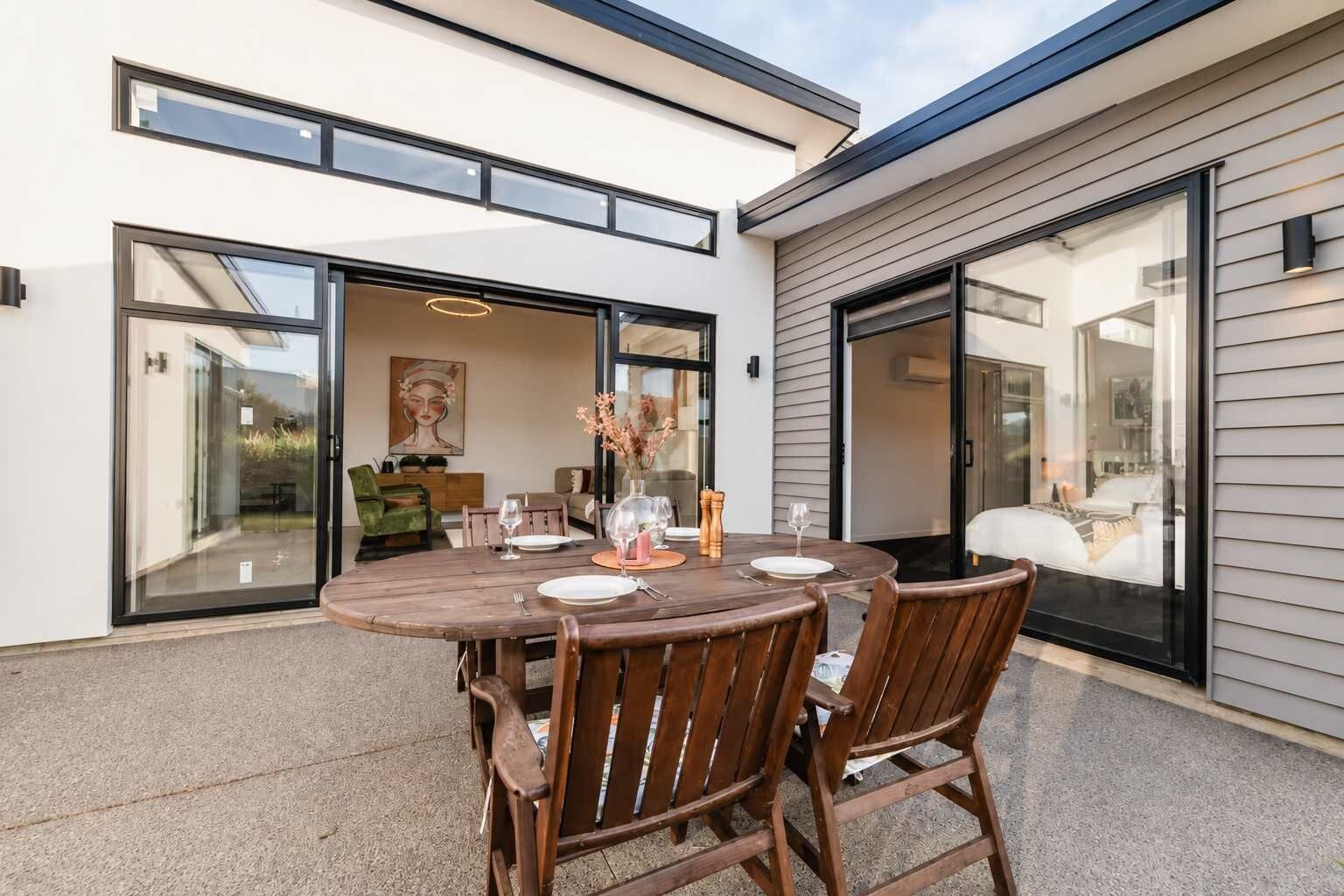 An outdoor dining area with a round table and chairs, a vase with flowers, and a painting on the wall.
